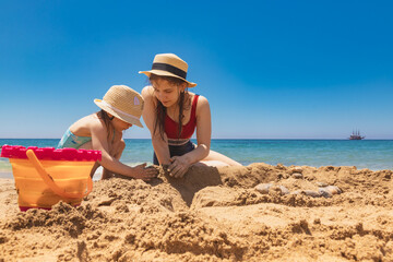 Sisters in sun hats building a sandcastle on a beach