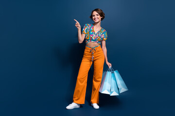 Full size photo of attractive young woman shopping bags point empty space wear trendy flared pants...