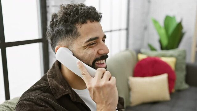 A bearded young man converses on a landline phone in a cozy, modern home, evoking a sense of casual communication.