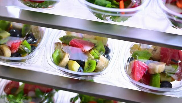 Plastic boxes with pre-packaged fruit and vegetable salads, put up for sale in a commercial refrigerator