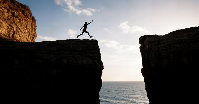Starting a business concept, making risks jumping a cliff. A silhouette of a man just running to jump on the other side.