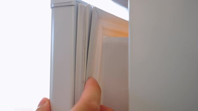 Close-up of a worn refrigerator seal with a crack. A hand shows a torn magnetic rubber band on the refrigerator door