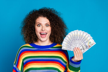 Photo portrait of lovely young lady hold money fan win lottery amazed wear trendy rainbow print garment isolated on blue color background