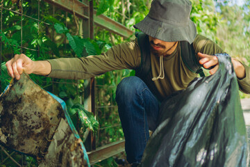 Latin man picking up garbage from an ecological reserve park, with a bag to clean the green areas
