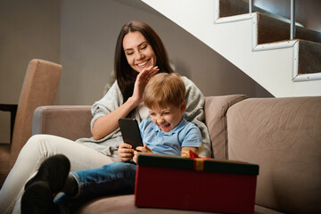 Laughing boy using smartphone with her mother on sofa celebrating Christmas