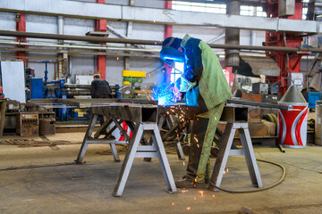A welder wearing a protective mask for metal welding and protective gloves performs welding work at...