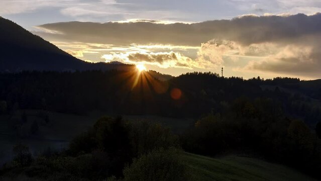 The setting sun behind the forested hills in the autumn landscape