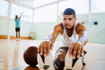 Young man stretching before playing basketball in an indoor basketball gym
