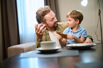 Father and son enjoy festive Christmas breakfast in hotel savoring gingerbread
