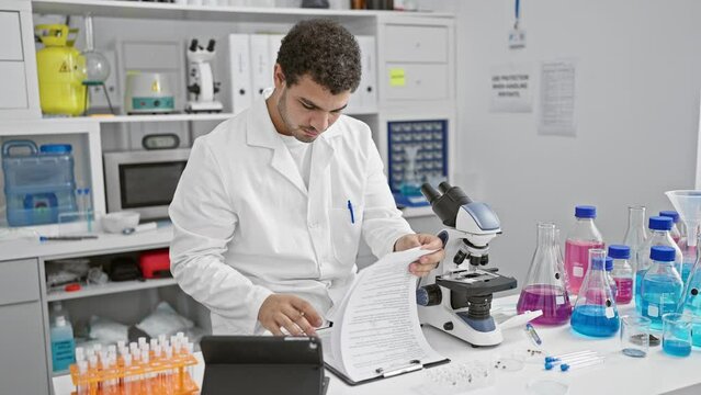 A focused male scientist examines a document beside a microscope in a modern laboratory.