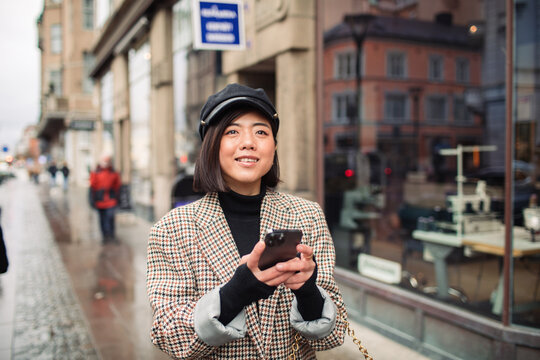 Smiling young trendy woman using smartphone on city walk