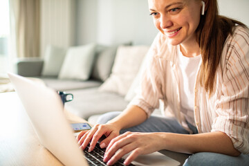 Smiling woman working on laptop at home with wireless earphones