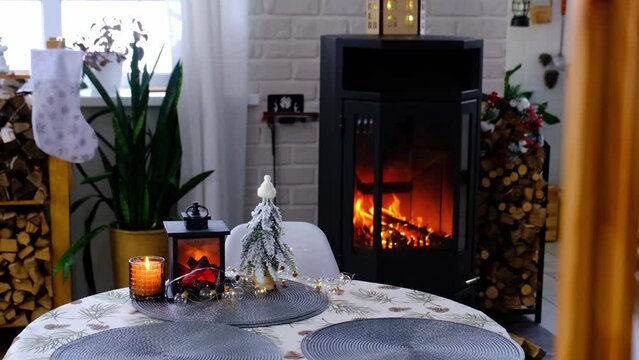 Metall black stove, burning hearth fireplace in white Festive interior of house is decorated for Christmas and New Year, Christmas tree. firewood in the woodpile, cozy and heating of home
