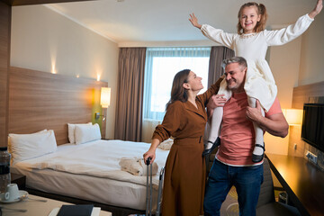 Obraz premium Mother caressing daughter with hands in air on father's shoulders in hotel room