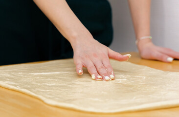 One Caucasian young girl greases the dough on the table with butter.
