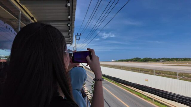 A woman stands and takes photos of a plane on the runway next to the airport as it slowly passes by.
People stand on the airport rice terrace to watch the planes.
runway background.