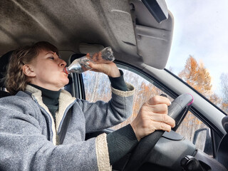 Portrait of female driver in solo journey. Adult mature woman holding steering wheel and bottle of water. Drinking while driving for to stay awake. Lady girl drinks alcohol vodka, gin while driving