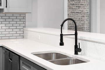 A kitchen faucet detail with grey cabinets, grey glass subway tile backsplash, and black faucet.