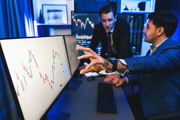Two stock investors discussing and pointing interesting market stock on monitor. Trend of the technology for dynamic economic investment for planning to select at neon light workplace. Sellable. - obrazy, fototapety, plakaty