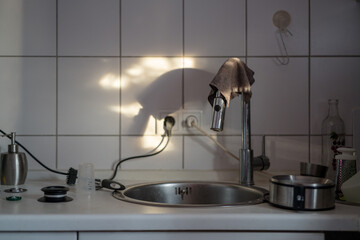 Stainless steel sink with tap and cleaning rags in the rising sun with light and shadow play in a kitchen