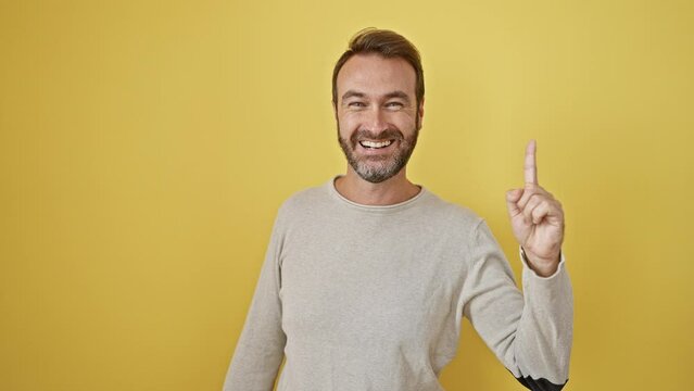 Young hispanic man standing pointing finger up with successful idea. exited and happy. number one. over isolated yellow background
