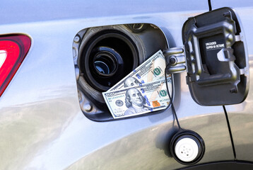 American dollars bills in the gas tank of a vehicle. Concept photo of the rising fuel price
