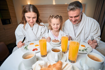 Obraz na płótnie Canvas European family having breakfast on bed at table in hotel room