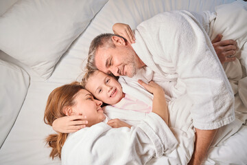 Fototapeta na wymiar Top view of happy family lying and hugging on bed in hotel room
