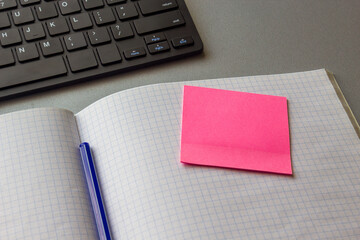 Open notebook with a pink sticky note and a blue pen on a desk with keyboard