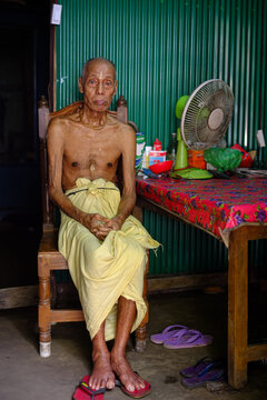 Bangladeshi rural elderly person sitting on a chair inside his home 