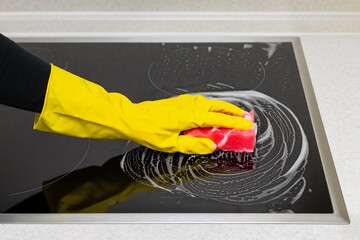woman in rubber gloves washes the hob in the kitchen.