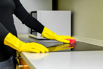woman in rubber gloves washes the hob in the kitchen.
