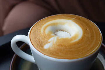 Close-up of a freshly brewed cappuccino with artistic foam art and sugar on it in a white cup
