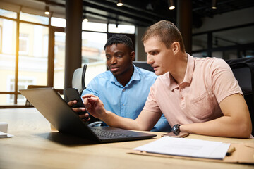 Caucasian man helping to African American colleague to adjust user interface