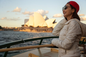 Asian female tourist carrying a travel backpack wearing a red hat stands in front of a boat...