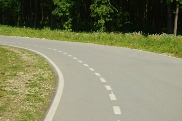 Asphalt road with road markings on an area with grass and trees on a summer day.