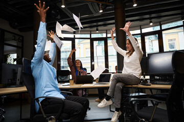 Happy multiethnic colleagues throwing papers up after successful brainstorm