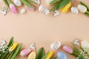 Fototapeta na wymiar Easter happiness concept. Top view flat lay of painted eggs, fresh tulips, cute easter bunnies on beige background with marketing space