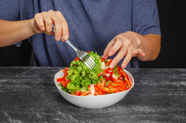 Chef stirs white bowl of freshly prepared tasty diet salad with a fork. Black background.