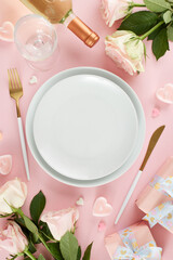 Luxurious Valentine's Day dining affair. Top view vertical photo of plates, cutlery, hearts, gift boxes, wine bottle, wine glass, roses on pastel pink background with promo zone