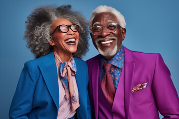 Cheerful laughing African American fashion senior man and asian woman having fun on studio background. Senior couple feeling vibrant in colorful casual clothing. Mature enjoying their golden years.