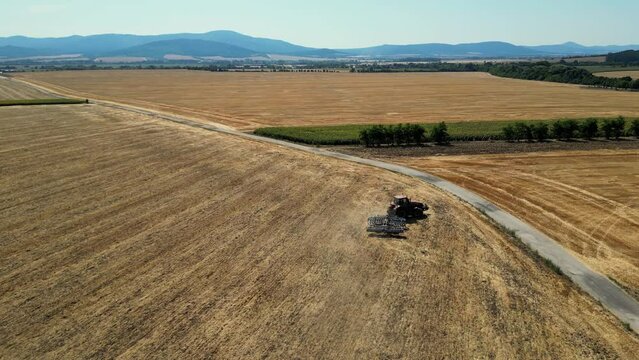 Flying over tractor with harrow system plowing ground on cultivated farm field. Industrial footage on agricultural theme. Agriculture in European country Slovakia. Blue Mountains in the background.