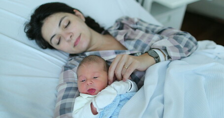 Obraz premium Mother holding newborn baby falling asleep together at hospital after birth in bed
