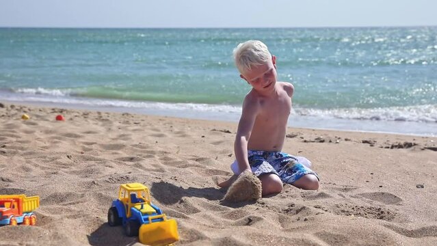 A cute little boy plays with sand and toys on the sandy beach near the sea. Summer time. Travel, Holiday and Adventure kids concept. Sand castle