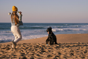 young beautiful woman on the beach plays with the big black dog giant schnauzer near the ocean 