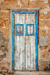 an old wooden door at the entrance of a seaside house. You can still see the original turquoise color, while the rest has been taken away by the salt