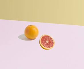 A grapefruit and a sliced grapefruit on a pink and ocher background. Minimal concept of fruit and...