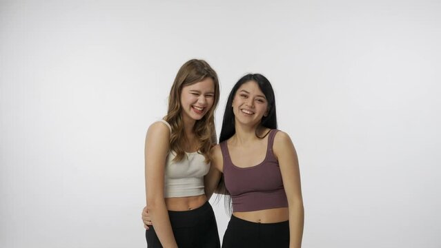Portrait of young multiracial models isolated on white studio background. Group of two attractive multiethnic girls talking laughing and joking. Multiethnic beauty concept.