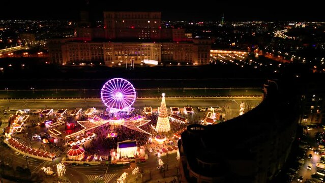 Aerial high angle drone shot holiday christmas market. Flyover biggest street market in Bucharest at night. Brightly lit celebration, shopping and food in Bucharest. Square decorated for new year 2025