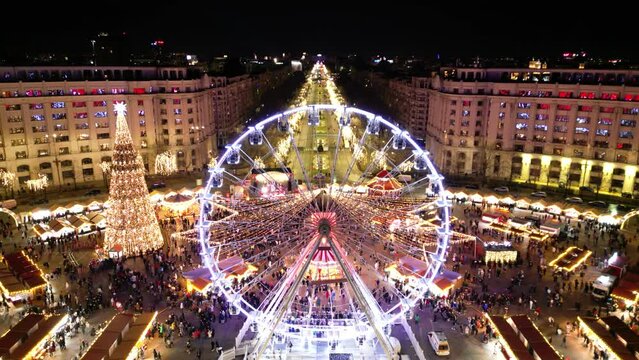 Aerial high angle drone shot holiday christmas market. Flyover biggest street market in Bucharest at night. Brightly lit celebration, shopping and food in Bucharest. Square decorated for new year 2025